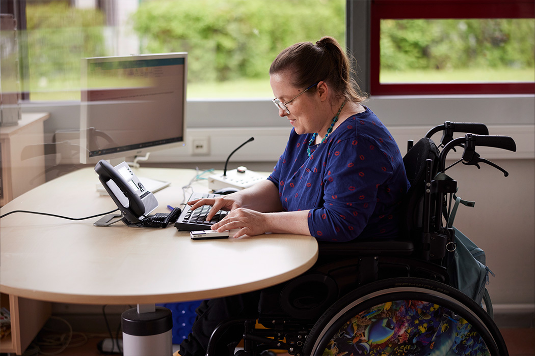 Eine Frau im Rollstuhl arbeitet in einem Büro